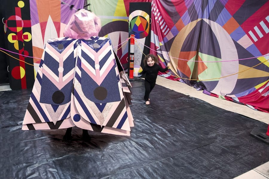 Costumed performer and toddler inside a colourful installation.