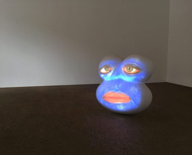 Tony Oursler's work titled 'Blue' an installation image. A circler blue form with human eyes and mouth.